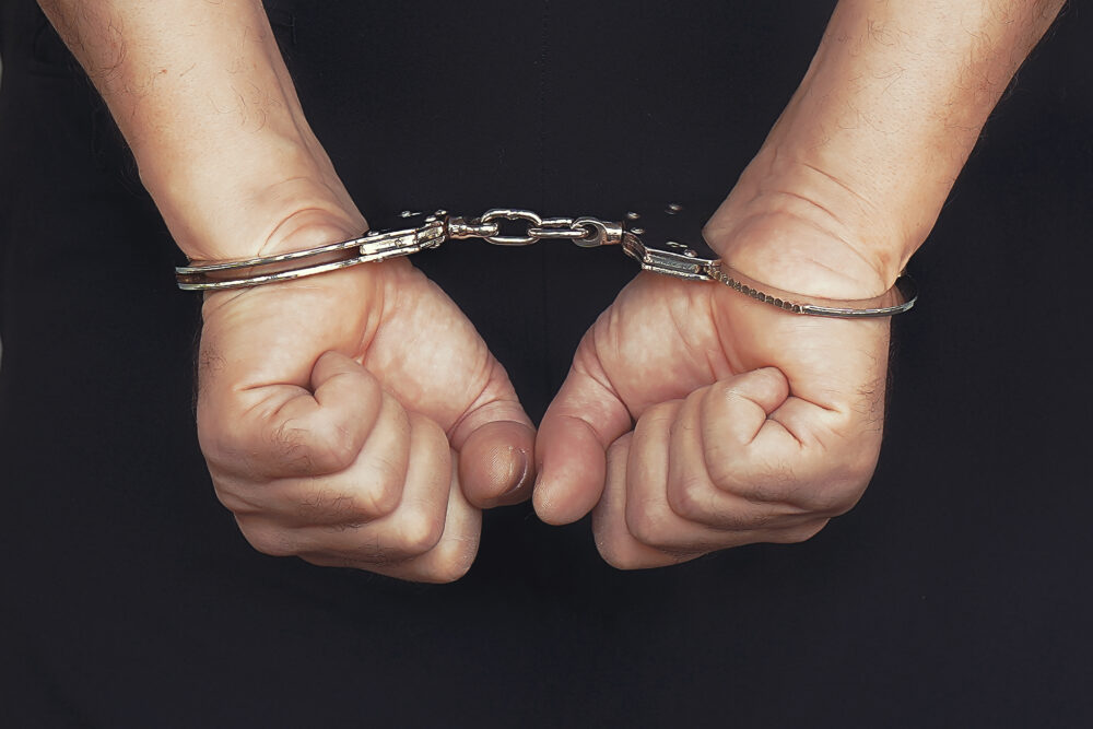 Arrested elderly man handcuffed hands at the back isolated on black background. Prisoner or arrested terrorist, close-up of hands in handcuffs. Toning